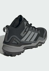 Baskets de sport noires et grises avec tige en mesh, design à trois bandes, semelle robuste et talon renforcé, dotées d'une languette pour un enfilage facile.