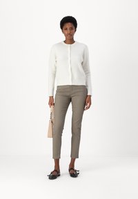 Vit stickad cardigan, beige slim-byxor, svarta ballerinas med rosetter och en liten beige handväska. Enkel design, slät textur och neutrala färger.