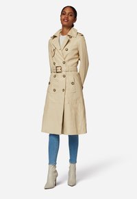Beige trenchcoat med dubbelknäppning, stora knappar, midjebälte och två framfickor. Matchad med ljusblå skinny jeans och ljusa stövlar.