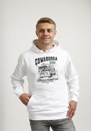 Young man wearing a white hoodie with black Teenage Mutant Ninja Turtles van graphic and text "Cowabunga TMNT powered by pizza."