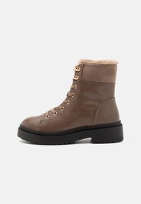 Bottines en cuir marron avec doublure en fausse fourrure, bout rond, semelle en caoutchouc noir et oeillets dorés pour les lacets.