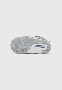 Schuhsohle aus strukturiertem grauem Gummi, mit einem kreisförmigen Muster und einem blauen "JORDAN"-Logo auf einem weißen Abschnitt.