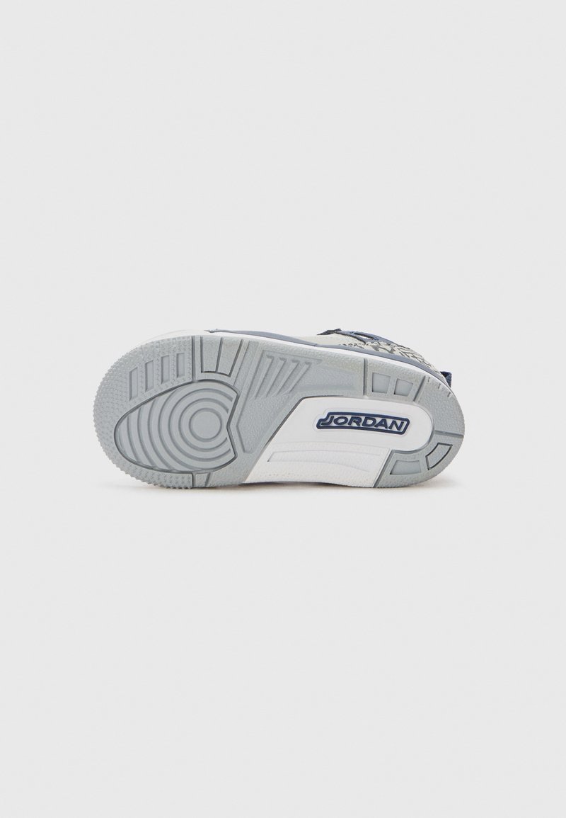 Suela de zapato con goma gris texturizada, que presenta un patrón circular y un logo azul de "JORDAN" en una sección blanca.
