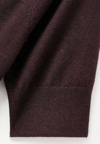 Bordo pulover sadrži meku, pletenu teksturu s rebrastim manžetama. Glatka površina s laganom dlačicom, naglašena za detalj.