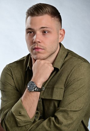 Olive green textured shirt with a collar and rolled sleeves, featuring a black watch with a stainless steel band on the wrist.