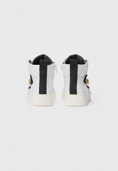 White high-top sneakers with a black rear panel, zip closures, and gold hardware accents. Textured soles for traction.