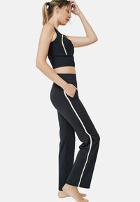 Zwarte sportbh met een diagonale crèmekleurige streep, gecombineerd met zwarte broek met een crèmekleurige zijstreep en een aansluitende tailleband. Textuurstof.