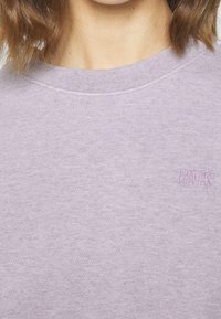 Sweatshirt girocollo lavanda realizzato in morbido tessuto. Presenta una superficie testurizzata e un piccolo logo ricamato Levi's sul petto.
