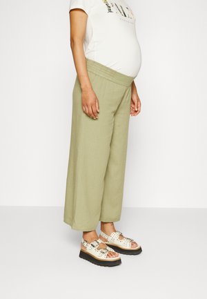 Calças largas de khaki claro com cintura elástica, combinadas com sandálias largas bege que apresentam recortes decorativos e uma sola preta.