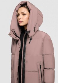 Chaqueta acolchada en rosa claro con una gran capucha, cierre de cremallera y detalles en negro. Cuenta con bolsillos laterales y una tela exterior texturizada.