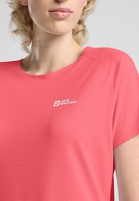 Maglietta a maniche corte, con scollo rotondo, di colore rosa brillante, realizzata in tessuto testurizzato. Presenta un logo bianco sul lato sinistro.