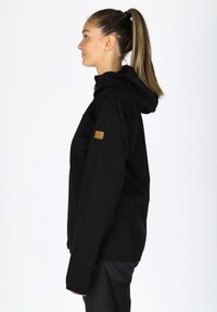 Svart huva jacka med en slimmad design, med en texturerad tyg och en distinkt brun logotyp på ärmen.