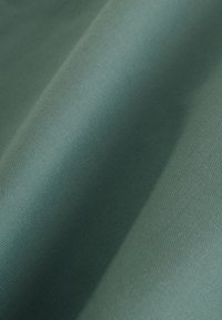 Gros plan sur un tissu bleu sarcelle lisse, tissé serré, avec des plis doux et un détail subtil de texture.