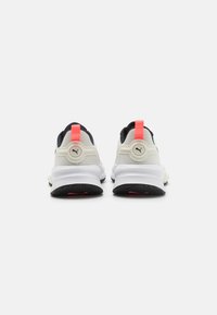 Zapatillas deportivas blancas y negras con una parte superior texturizada, acentos rojos y una suela de goma con un patrón de relieve. Diseño de talón reforzado.