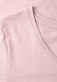 Blødt lyserødt V-hals bomuldsstof med fine syningsdetaljer langs halsudskæringen og skuldersømmen.