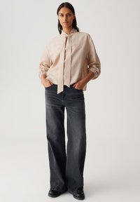 Cream-colored blouse with a tie detail, long sleeves, and textured fabric. Paired with dark gray wide-leg jeans and black shoes.