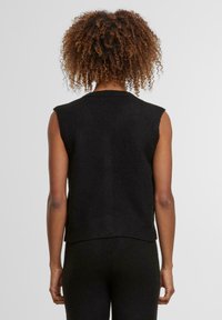 Černý bezrukávový pletený svetr s vroubkovaným lemem a jemnou texturou. Jednoduchý design bez zapínání, vhodný na vrstvení.