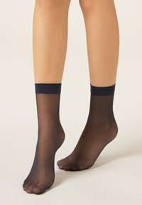 Calze alla caviglia nere velate con bordo elastico scuro, tessuto liscio e design a punta aperta, che offrono un aspetto leggero per il massimo comfort.