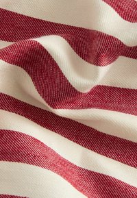 Tissu à rayures rouges et crème avec un tissage texturé, affichant des rayures larges et étroites alternées, mettant en évidence une apparence douce.