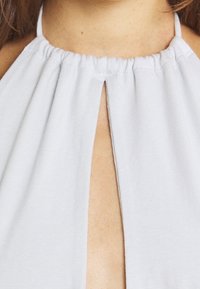 Ljust grå halterneck-top i mjukt tyg, med samlad halsringning, framåtriktad nyckelhålskut och slät yta.