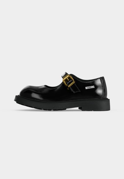 Chaussure Mary Jane noire brillante avec semelle épaisse et bride à boucle dorée, avec logo Moschino sur le talon.
