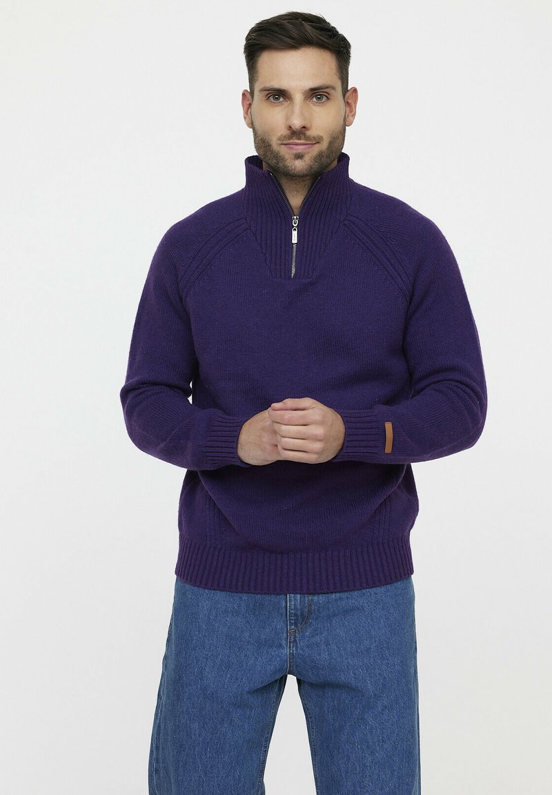 Pull en laine violet avec un col zippé demi-long, des poignets et un ourlet côtelés, arborant un motif texturé subtil, porté sur un jean en denim bleu.