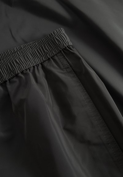 Μαύρο παντελόνι με ελαστική μέση και εμφανείς ραφές σε φόντο από λείο ύφασμα.