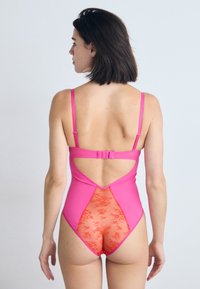 Roze tankini met verstelbare bandjes, voorzien van een kanten gaas inzet in contrasterend oranje aan de achterkant. Glad stofafwerking.