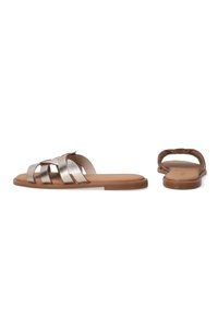 Flade sandaler med et metallic sølvremdesign, brun sål og åben ryg. Glat tekstur med en minimalistisk, vævet remdetalje.