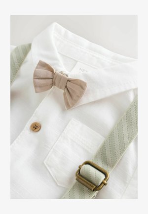 Biała koszula z kołnierzykiem z beżowym krawatem w kokardę, drewnianym guzikiem i zielonymi szelkami w paski, zabezpieczonymi mosiężnymi zapięciami. Proste detale dotyczące tekstury.
