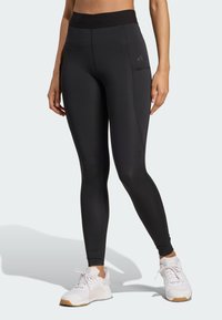 Leggings sportivi neri con vita alta, realizzati in materiale elasticizzato. Presentano una tasca laterale e dettagli di cucitura a contrasto.