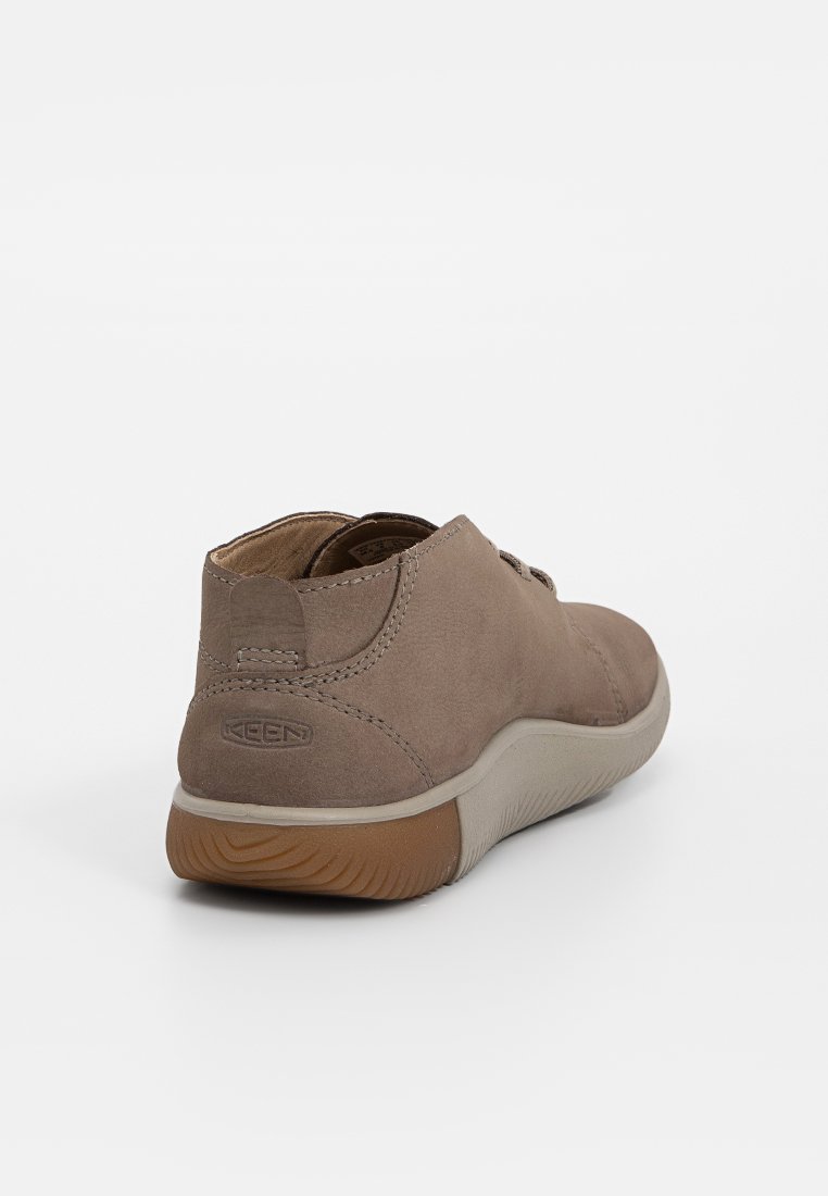 Brązowe zamszowe buty o zaokrąglonym kształcie, z lekką gumową podeszwą i subtelnymi detalami w postaci przeszyć. Wytłoczone logo na tylnej części.