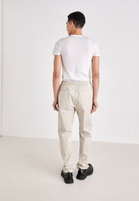 Beige, lette bomuldsbukser med elastisk talje og sidelommer. Kombineret med en tætsiddende hvid T-shirt med rund hals og sorte sko.