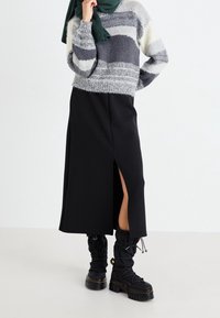 Jupe noire avec une fente haute jusqu'à la cuisse, associée à un pull rayé gris et blanc et des bottes noires lacées jusqu'aux genoux. Texture en laine.