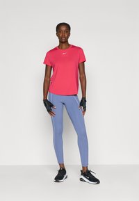 Camiseta roja de Nike, de mangas cortas; leggings azul claro con tiras laterales blancas; zapatos deportivos negros; guantes negros sin dedos.