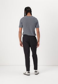 Rutet grå T-skjorte med korte ermer, kombinert med svarte smale bukser og sandaler med åpen hæl, sett fra baksiden. Enkelt design og avslappet passform.