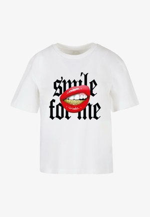 Valge puuvillane T-särk, millel on graafiline kujundus punastest huultest nähtavate hammaste ja kuldsete breketitega, mille all on must kiri "naerata minu jaoks."