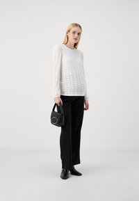 White, patterned blouse with a textured design and puffed sleeves, paired with black, straight-leg trousers and a small black handbag.