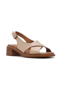 Sandale slingback en cuir beige avec brides croisées, bout ouvert, boucle réglable et petit talon bloc empilé sur semelle couleur camel.
