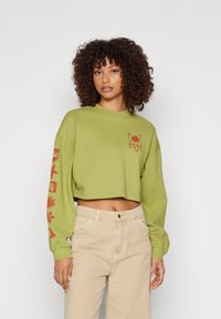 Cropped green sweatshirt with long sleeves. Features orange floral graphics on the front and sleeve. Made from soft fabric.