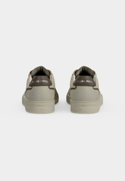 Paire de baskets beiges avec des accents marron au talon et le texte "Filling Pieces" à l'arrière, vues de dos sur un fond uni.