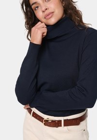Navy turtleneck sweater with ribbed texture, long sleeves, paired with a brown crocodile-patterned belt and light-colored pants.