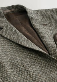 Blazer din amestec de lână în model ghepard maro și gri. Are un guler cu decupaj și căptușeală cu model maro. Se observă două buzunare frontale.