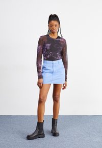 Haut en maille noire à manches longues avec un motif violet, associé à une mini-jupe en denim bleu clair et des bottines noires, avec des matériaux texturés.
