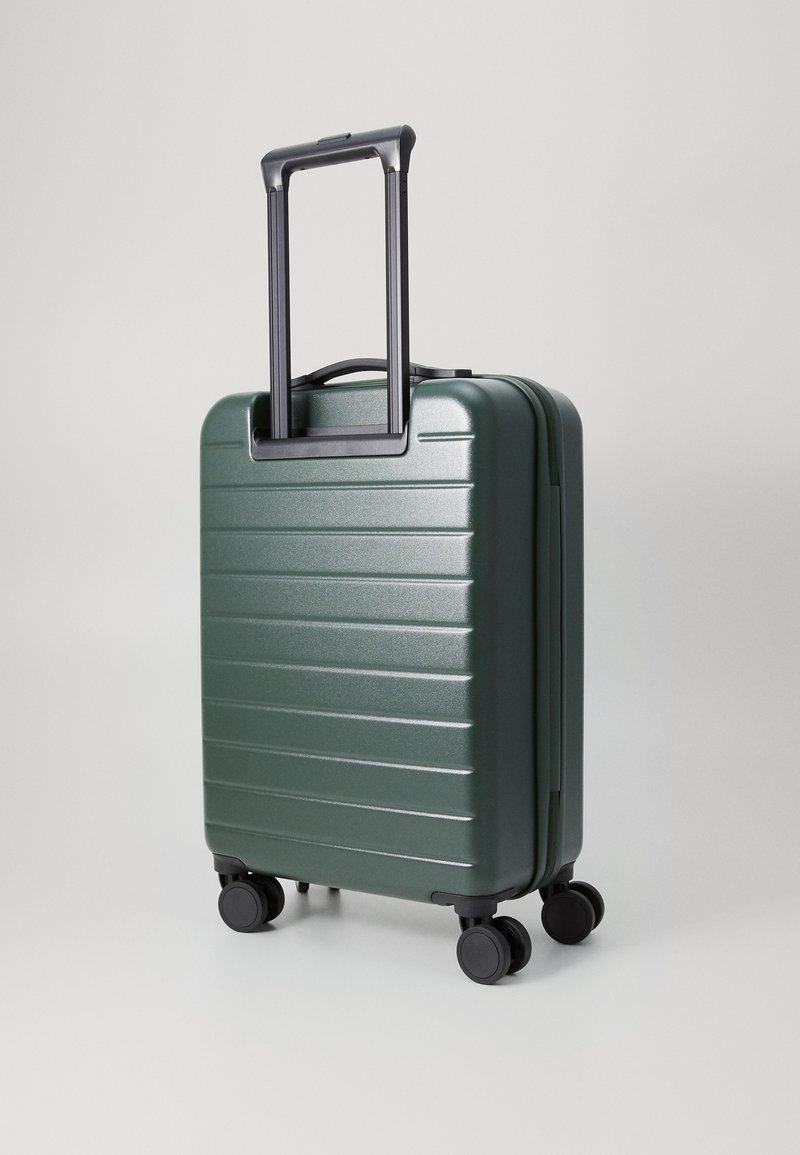 Maleta rígida de color verde oscuro, con una superficie texturizada y ranuras horizontales, un asa negra retráctil y cuatro ruedas negras suaves.