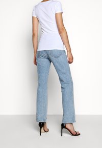 Vit kortärmad t-shirt kombinerad med ljusblå raka jeans och svarta högklackade sandaler, vilket framhäver en avslappnad look med en figurnära silhuett.