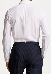 Witte blouse met lange mouwen en een klassieke kraag, voorzien van manchetten met knopen. Gecombineerd met donkere broek met fijne krijtstrepen. Strakke, getailleerde pasvorm.