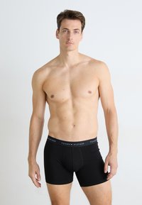 Boxer-briefs noirs en tissu doux avec une ceinture élastique de marque en noir avec des accents rouges et blancs. Conception basique, sans motifs.