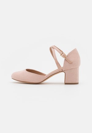 Chaussure unique en daim rose clair à petit talon avec bout arrondi et doubles fines brides à la cheville avec petite boucle dorée sur fond blanc.