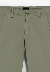 Pantalones de un suave verde oliva hechos de una tela blanda. Incluyen un cierre de botón, bolsillos frontales y sutiles detalles de costura.